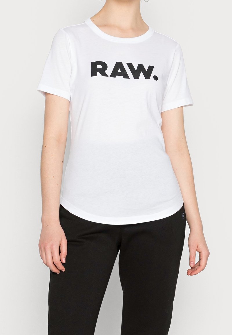 Bílá krátká rukávová tričko vyrobené z bavlny, s velkým černým grafickým prvkem "RAW." přes hruď, kulatým výstřihem a zaobleným lemem.