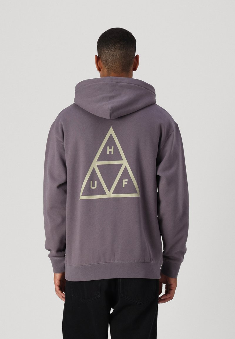 Sudadera con capucha gris que presenta un gran logotipo triangular con "H", "U" y "F" en color crema. Tejido suave con puños y dobladillo acanalados.