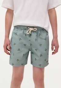 Pantaloni da bagno in tessuto verde chiaro, con motivo teschio e tibie. Vita elastica con lacci beige. Vestibilità casual.