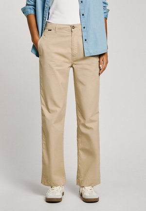 Pantalones de pierna ancha beige, hechos de algodón, con cierre de botón, bolsillos laterales y corte estándar, combinados con zapatillas blancas.