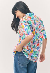 Kurzärmliges Hemd aus leichtem Stoff, mit einem bunten Blumen- und Tiermuster auf weißem Hintergrund. Lockerer Schnitt mit Kragen.
