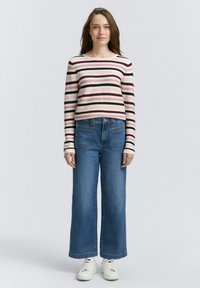 Dryžuotas ilgos rankovės marškinėliai kreminės, raudonos ir juodos spalvų; derinami su plačiais mėlynais džinsais ir baltais sportbačiais, demonstruojantys kasdienį stilių.