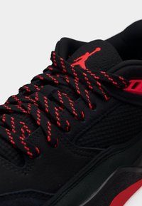 Μαύρο αθλητικό παπούτσι με υφή στην επιφάνεια, κόκκινα κορδόνια ως διακοσμητική λεπτομέρεια και ορατό λογότυπο. Διαθέτει επενδεδυμένο γιακά και στιλιζαρισμένο σχέδιο σόλας.