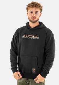 Sudadera de algodón negra con un bolsillo tipo canguro, con una impresión gráfica "KAPORAL URBAN DENIM". Puños y cintura acanalados. Etiqueta de logo prominente.