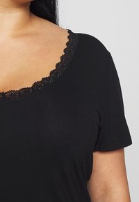 Svart t-shirt med korta ärmar och rund halsringning, med en scalloped spetskant. Mjuk tyg med en lätt lyster.