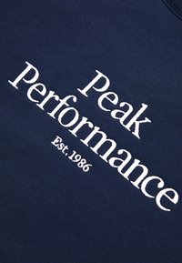 Marineblauwe sweatshirt met witte geborduurde tekst "Peak Performance" en "Est. 1986." De stof lijkt zacht met een gladde textuur.