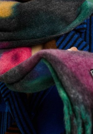 Personne enveloppée dans des couvertures en laine colorées et douces, superposées sur un vêtement rayé bleu et noir.