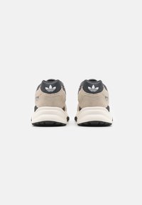 Sneaker beige e nere con tomaia in camoscio, colletto imbottito e suola in gomma. Presentano il logo sul tallone e un design minimalista.