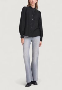 Camicia nera con bottoni, collo arricciato e maniche lunghe a palloncino. Abbinata a jeans grigi chiari a gamba svasata e stivaletti neri alla caviglia.