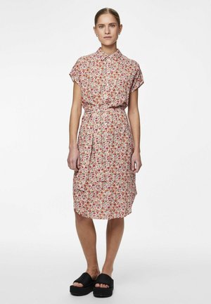 Abito a camicia con motivo floreale in rosso e verde su uno sfondo chiaro, maniche corte, vita con cintura e taglio a lunghezza ginocchio. Sandali neri piatti.