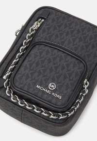 Borsa a tracolla nera con texture, accentuata da una catena argentata, dotata di un compartimento principale con zip e di una tasca frontale. Logo ben visibile.