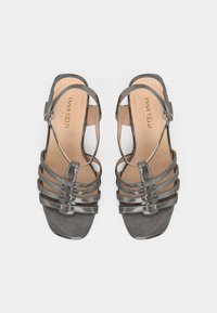 Pelēkas zamšādas sandales ar četrām šaurām siksnām un pirksta cilpiņu dizainu. Tām ir sprādzes stiprinājuma apavstīga siksniņa un teksturēta zolīte. Kvadrātveida pirkstu forma.