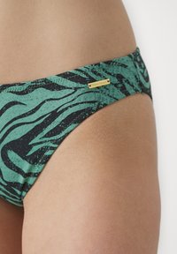 Zeleno bikinki dno s črnim valovitim vzorcem in zlatim logotipom. Narejeno iz gladkega materiala z nizkim rezom.