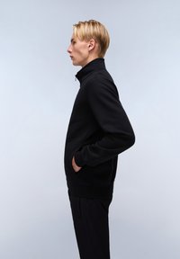 Černá mikina na zip s vysokým límcem, dlouhými rukávy, bočními kapsami a žebrovanými manžetami; vyrobena z měkké tkaniny s hladkou texturou.