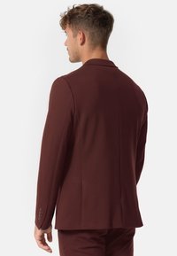 Bordeauxfarbener Blazer mit taillierter Passform, strukturierten Schultern, glattem Stoff und einem Schlitz hinten. Einfache Knopfdetails an den Ärmeln.