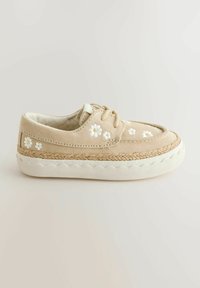 Chaussure en suède beige avec broderie florale blanche, détail en jute tressé à la semelle et semelle extérieure en caoutchouc blanc. Bout arrondi et laçage.
