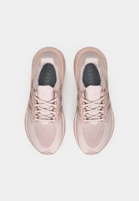 Pár bledě růžových běžeckých bot Adidas Ultraboost zobrazených shora na bílém pozadí.