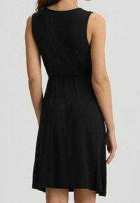 Musta hihaton mekko, jossa on istuva vyötärö ja levenevä helma. Valmistettu sileästä kankaasta, yksinkertaisella designilla ilman näkyviä kuvioita tai koristeita.