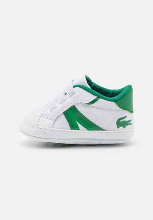 Weißes Kindersneaker mit grünen Akzenten, strukturiertem Canvas-Material, elastischen Schnürsenkeln und einem Logodetail an der Ferse. Niedriges Design.
