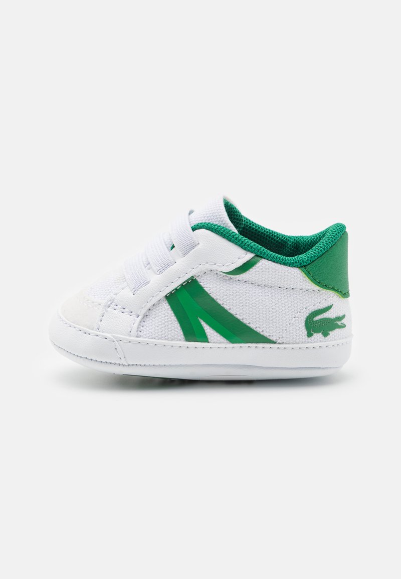 White children's sneaker with green accents, textured canvas material, elastic laces, and a logo detail on the heel. Low-rise design.