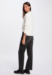 Maglione lavorato a maglia color avorio con collo a camicia, abbinato a jeans grigio scuro a vita alta e calzature nere. Design semplice, vestibilità comoda.