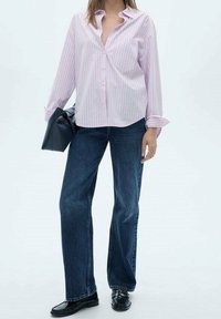 Chemise à rayures roses claires avec boutons et manches longues, associée à un jean bleu à jambes larges et des chaussures noires. Accessoires : un sac noir.