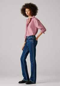 Sarkani un baltu svītru krekls ar uzruļētām piedurknēm, kopā ar tumši zilām uzplūdušām džinsām. Tērpam ir melni apavi un brīva pozīcija.