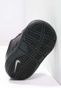 Černá sportovní podrážka s texturovanou gumou pro záběr, vyznačující se charakteristickým vzorem rybí kosti a stříbrným logem Nike swoosh.