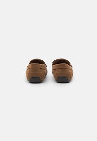 Brown suede slip-on shoes with a rounded toe, low back, and black rubber sole, showcasing stitched detailing and a smooth texture.