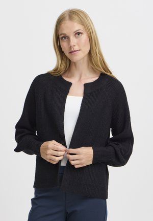 Black knitted cardigan with a textured finish, open front, round neckline, and long, slightly puffy sleeves. Paired with a white top.