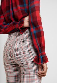 Chemise à manches longues à carreaux rouges et bleus avec poignets boutonnés, associée à un pantalon taille haute à carreaux noir et blanc avec poches.