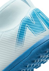 Primer plano de una zapatilla deportiva texturizada blanca y azul con una suela estampada y un gran logotipo azul en el costado.