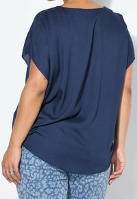 Haut bleu marine à manches courtes avec une coupe ample et un ourlet arrondi, associé à un jean bleu clair à motif avec un design abstrait subtil.