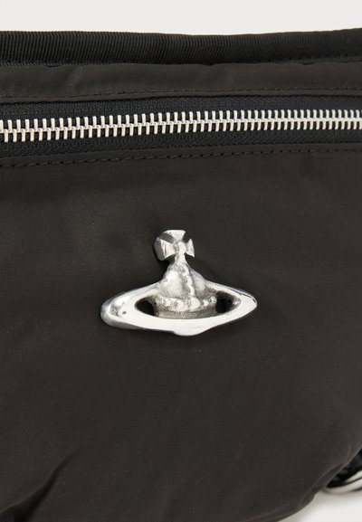 Ασημένιο έμβλημα σφαίρας και σταυρού σε μαύρο ύφασμα κοντά σε οριζόντια ασημένια φερμουάρ, πιθανώς σε τσάντα ή θήκη.