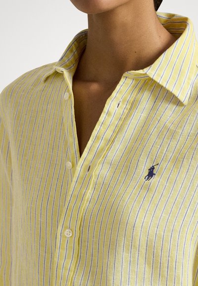 Dzeltena un balta svītraina krekliņa ar pogām un apkakli, uz krūtīm mazs tumši zils izšūts polo spēlētāja logotips.