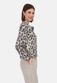Langärmliges Oberteil mit Leopardenmuster in Beige und Grau, mit Rundhalsausschnitt und entspannter Passform. Weicher Stoff mit Knopfdetail am Hals.