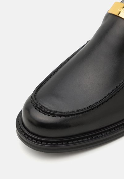 Must musta loafer musta ümmarguse varbaga, stiilse kujuga, peent õmblusdetaili ja kuldse metallilise aktsendiga. Sile tekstuur kogu ulatuses.