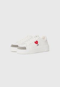 White sneakers featuring a smooth leather upper with a grey suede toe cap, decorative red heart graphic, and "LOVE" text, flat laces, and thick sole.
