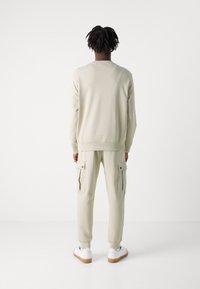 Sudadera color beige claro y pantalones cargo con bolsillos, hechos de una tela suave, con puños acanalados, y combinados con zapatillas blancas.