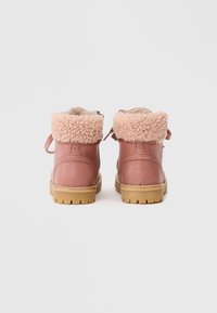Botas de tornozelo rosa em couro, com um colarinho suave e felpudo na mesma tonalidade, atilhos na parte traseira e uma sólida sola de borracha castanha com estruturas para aderência.