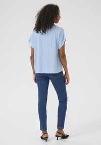 Blouse à manches courtes bleu clair en tissu doux, assortie à un jean bleu ajusté et des sandales à talons noires, vue de dos.