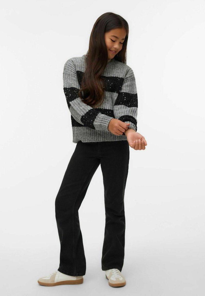 Szary i czarny sweter w paski z dzianiny o fakturowanej tkaninie, zestawiony z czarnymi rozszerzanymi dżinsami oraz białymi trampkami z gumowymi podeszwami.