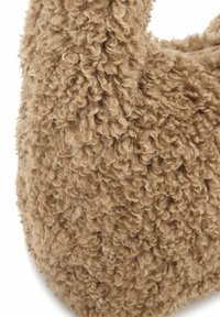 Tissu texturé brun avec une apparence bouclée et pelucheuse, formant une forme arrondie. La surface douce et duveteuse améliore l'expérience tactile.