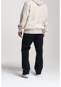 Kremowa bluza z kapturem o luźnym kroju, z regulowanym sznurkiem w kapturze, zestawiona z czarnymi dżinsami i białymi trampkami z marmurkowym akcentem.