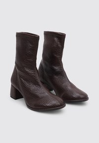 Botas de tobillo de cuero marrón con un acabado texturizado, punta cuadrada y tacón cuadrado. Diseño sin costuras con un estilo minimalista.