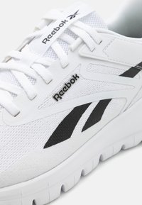 Fehér sportcipő hálós felsőrésszel, fekete Reebok logóval és fekete részletekkel. Vastag fehér talppal rendelkezik, amely texturált profillal és kerek cipőfűzőkkel van ellátva.