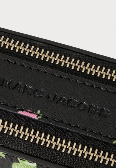 Κοντινή λήψη φερμουάρ σε μαύρη τσάντα Marc Jacobs με μεταλλικά δόντια και ραμμένη μαύρη δερμάτινη επένδυση που δείχνει μέρος ενός λουλουδάτου σχεδίου.