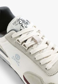 Scarpa sportiva bianca realizzata in un mix di tessuto e suede, con dettagli grigi e logo a teschio. La punta arrotondata e i lacci piatti completano il design.