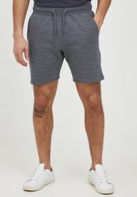 Grå træningsshorts med en struktureret stof, snøre i taljen og et subtilt mønster. Bærer hvide sneakers.