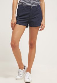 Pantalones cortos de algodón azul marino con un frente plano, bolsillos clásicos y cierre de botón. Presenta un corte slim y dobladillos en las piernas.